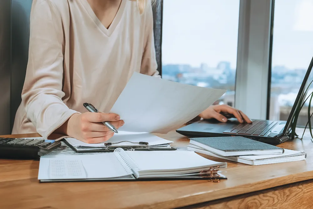 Reviewing a printed financial report beside an open laptop