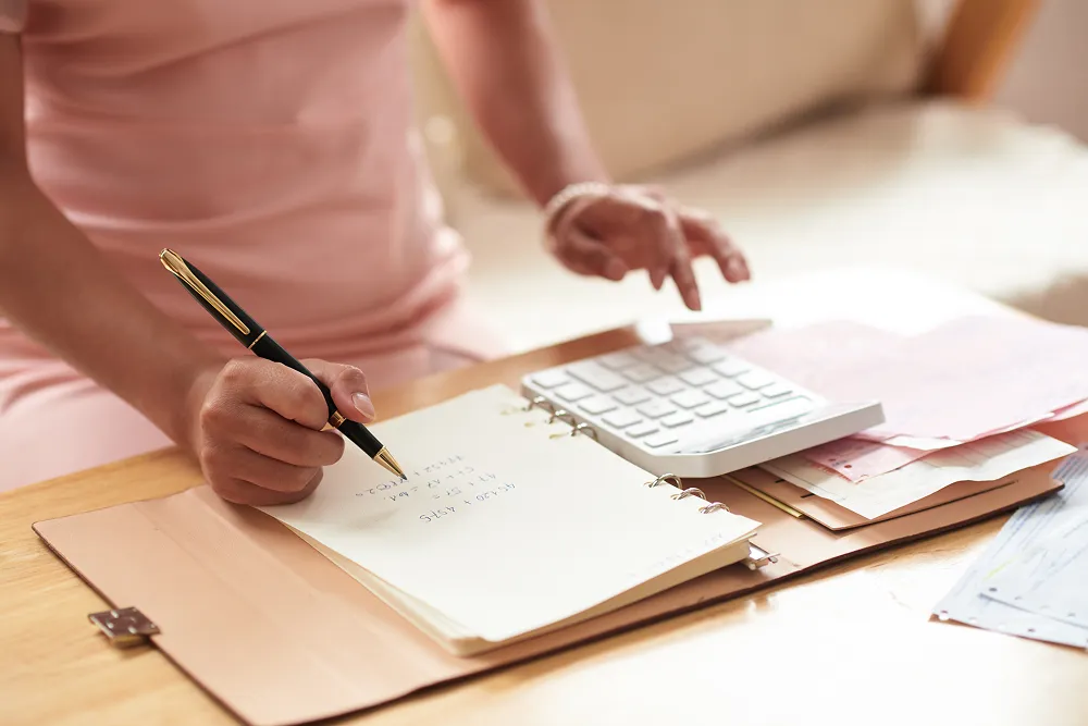 Writing figures in a ring binder beside a calculator and receipts
